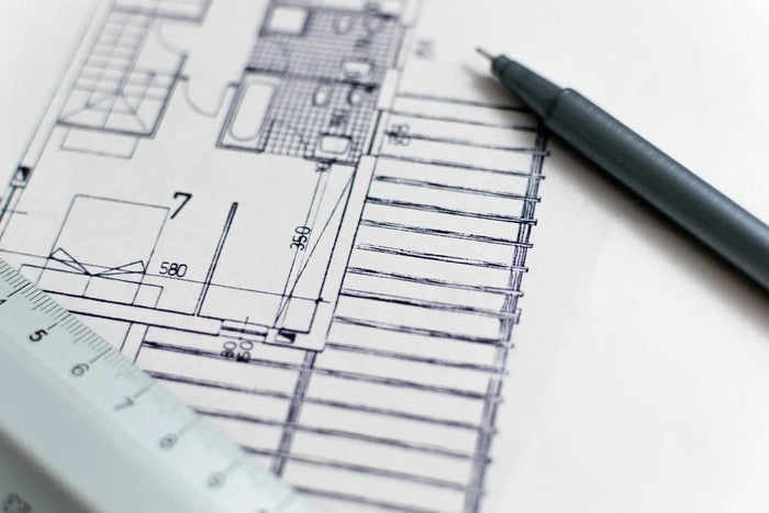 A black ink pen with a matte gray barrel resting diagonally on architectural blueprints for building permit costs and site plan