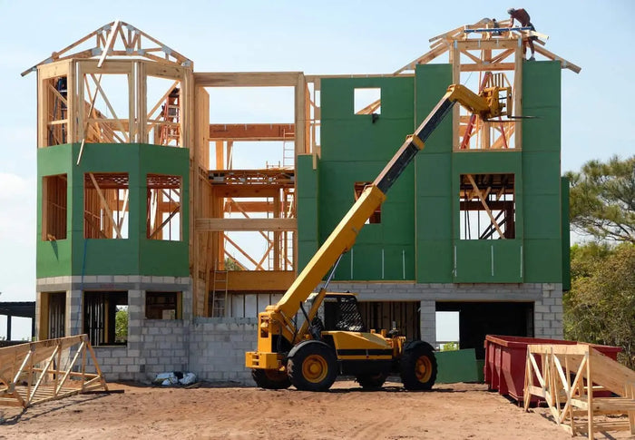 Yellow telescopic boom lift parked on a construction site supporting site plan and interior trim installation.