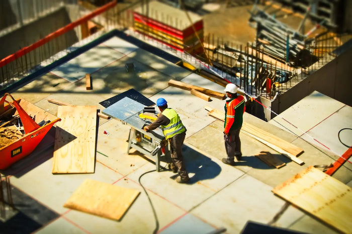 A worker in a blue hard hat and high-visibility vest operates a table saw on a residential development project site.