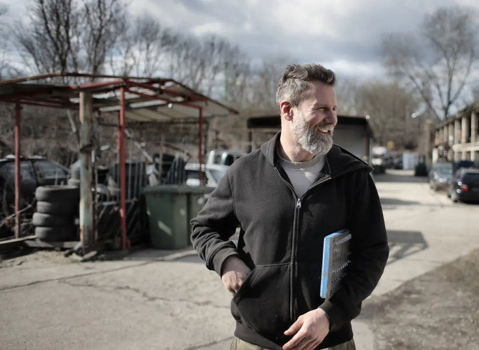 Man wearing black zip-up hoodie with gray undershirt holding blue notebook in a construction project for general contractors.