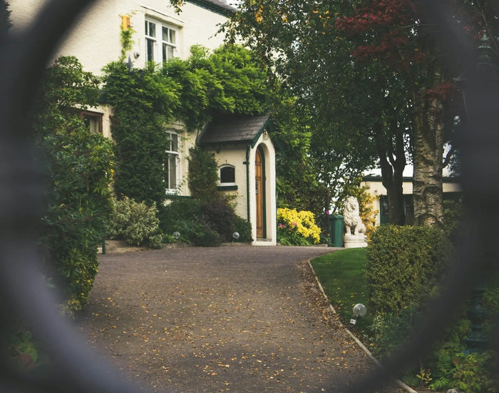 A white stone house with ivy walls and wooden door surrounded by greenery illustrating site plan and driveway materials.