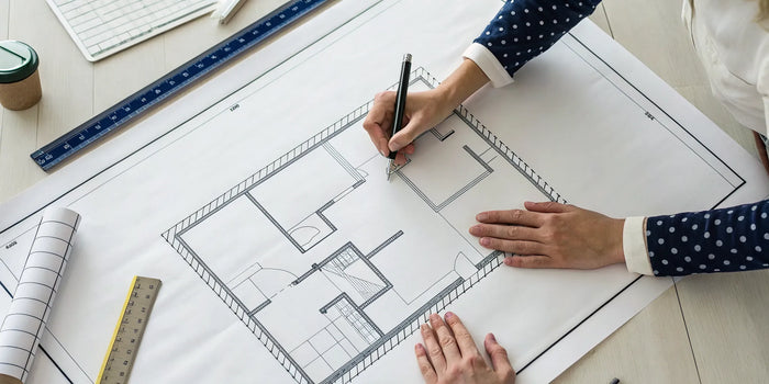 A professional drafts a property plot plan on a blueprint with a ruler and pencil.