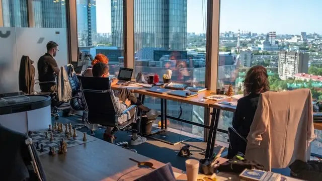 Modern office layout with open floor plan and large windows overlooking cityscape featuring people working at desks