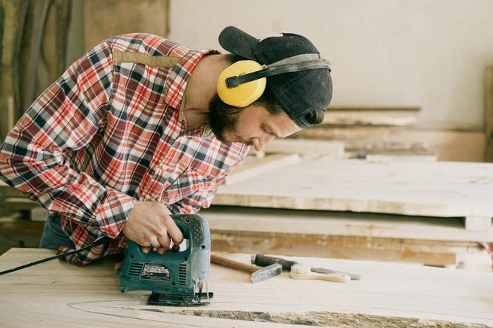 A person operating a teal and black electric jigsaw with blade in a workshop for a general contractor construction project.