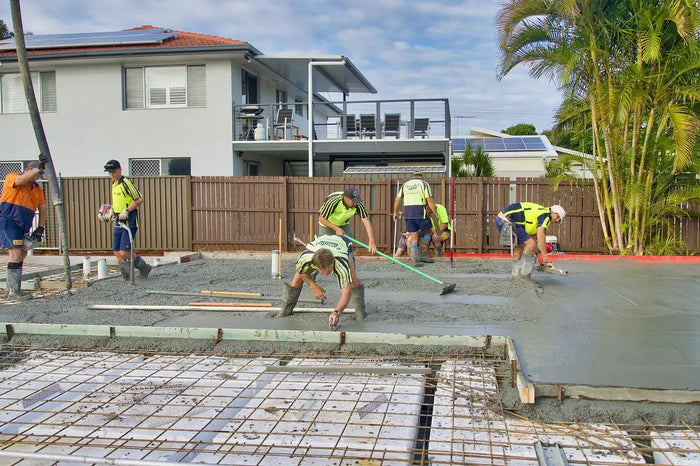 Workers in high-visibility vests spreading wet concrete on a construction site illustrating slab vs crawl space concepts.