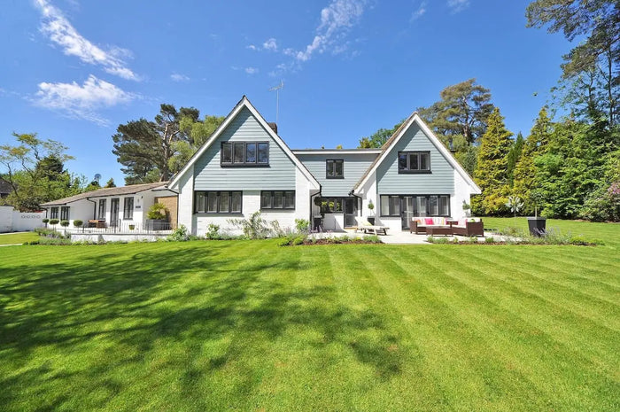A modern two-story house with light blue siding and black windows showcasing residential landscape design with a green lawn.