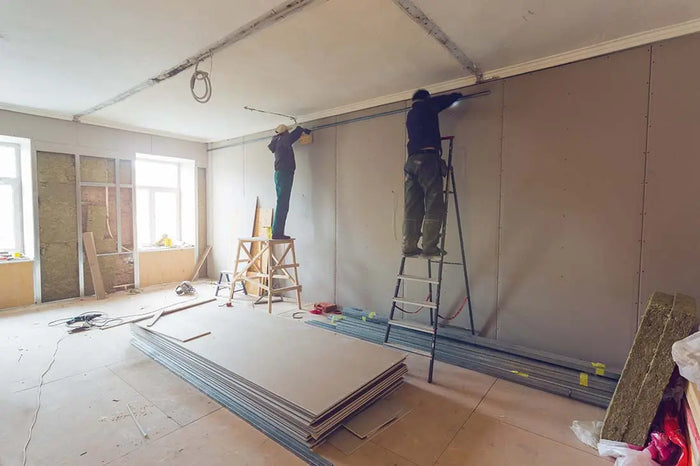 Two workers installing drywall panels in a home remodeling project for a room under construction.