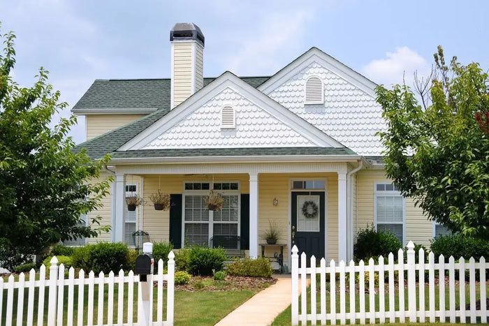 A charming yellow house with white siding black shutters and dark green roof illustrating a house site plan example.