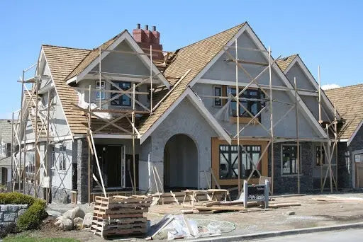 A gray two-story house under construction with brown shingled roof and scaffolding illustrating site plans and property lines