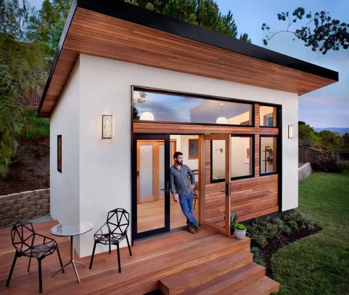 Modern minimalist accessory dwelling unit with white stucco walls, dark wood accents, and black-framed glass doors to wooden deck