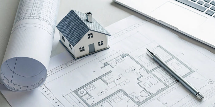 A miniature house and blueprint on a desk for a homeowner's my site plan.