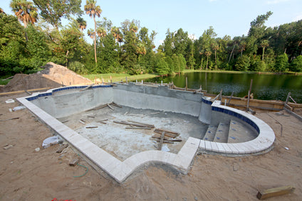 blue rectangular swimming pool under construction with yellow excavators and workers using a site plan for demolition